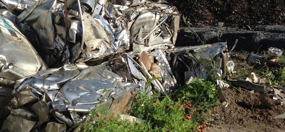 Bales of scrap metal stacked near wildflowers